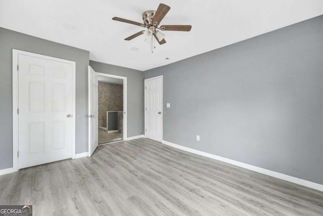 unfurnished bedroom with baseboards, ensuite bathroom, wood finished floors, and a ceiling fan