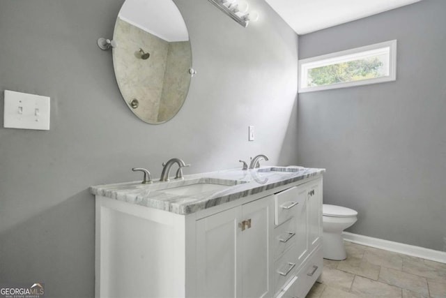 full bath with baseboards, toilet, double vanity, and a sink