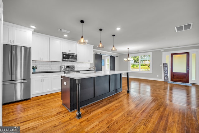 68 Hayes St, Toccoa, GA 30577 - kitchen featuring appliances with stainless steel finishes, ornamental molding, white cabinetry, light wood-type flooring, and a center island with sink