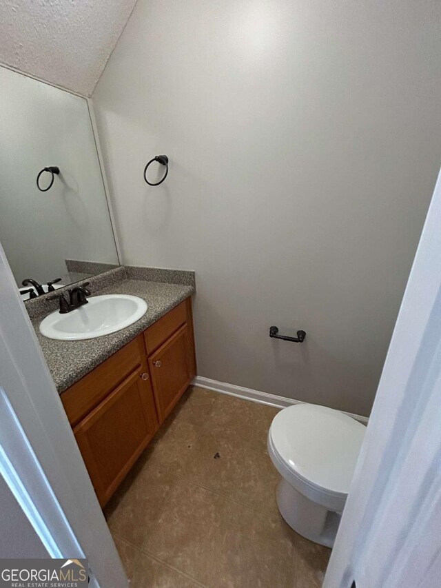 half bathroom with toilet, vanity, baseboards, and a textured ceiling