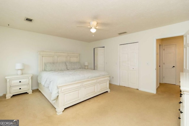 bedroom with baseboards, multiple closets, visible vents, and light carpet