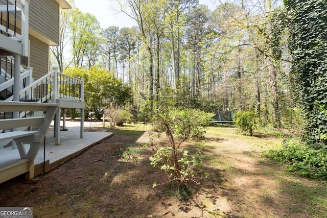 view of yard featuring stairs, a trampoline, a wooden deck, and a patio area