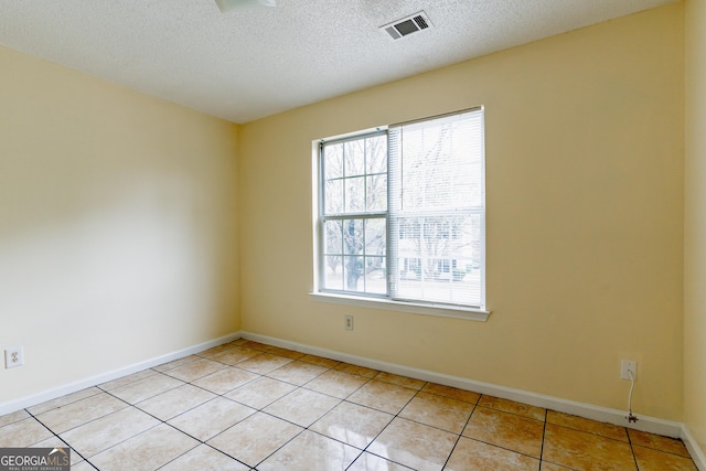spare room with a textured ceiling, visible vents, light tile patterned floors, and plenty of natural light