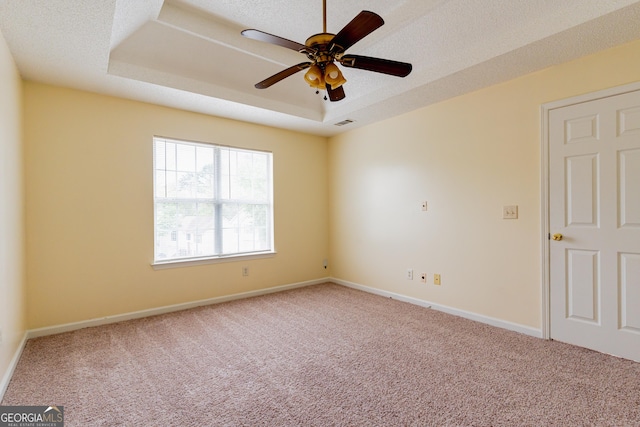 spare room with a textured ceiling, carpet, baseboards, ceiling fan, and a tray ceiling