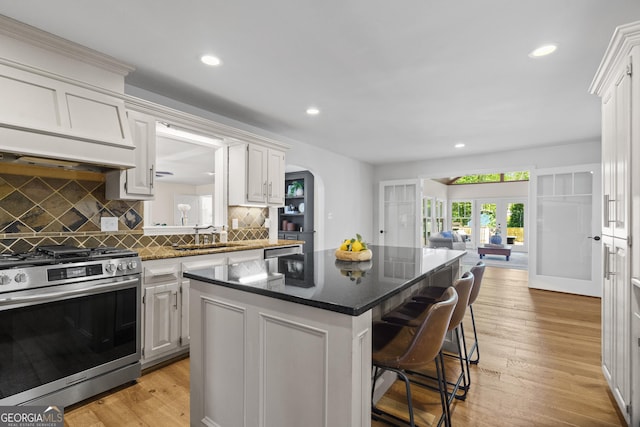 kitchen featuring a center island, a sink, a kitchen bar, french doors, and stainless steel gas range oven