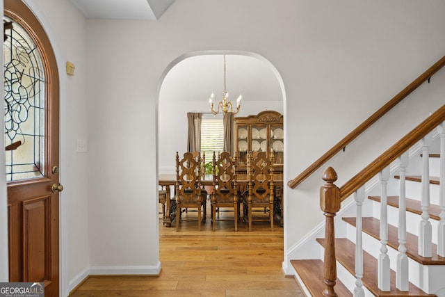entrance foyer with baseboards, a chandelier, light wood-style flooring, stairs, and arched walkways