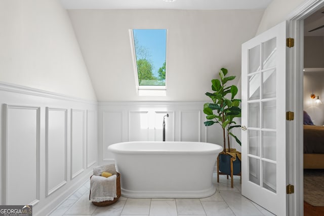 full bathroom featuring a decorative wall, wainscoting, a freestanding tub, and lofted ceiling
