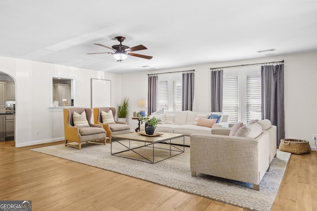 living area with visible vents, baseboards, arched walkways, ceiling fan, and light wood-style flooring