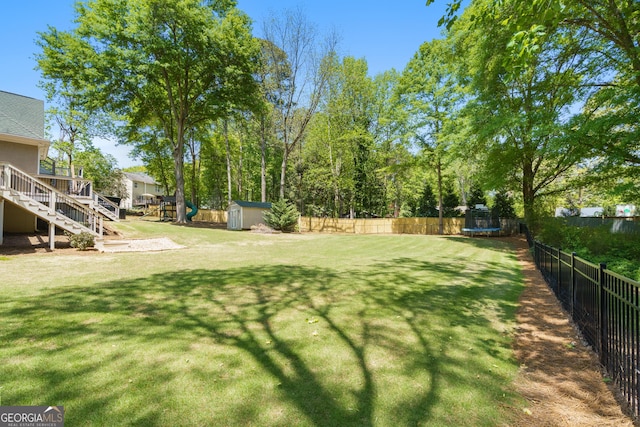 view of yard featuring a trampoline, an outdoor structure, stairway, a fenced backyard, and a storage shed