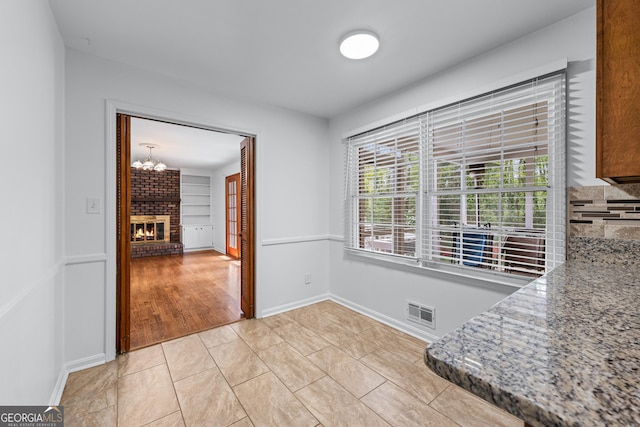unfurnished dining area with light tile patterned floors, baseboards, visible vents, a chandelier, and a fireplace