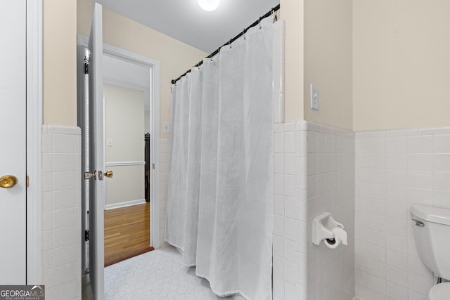 full bath featuring toilet, tile walls, and wainscoting