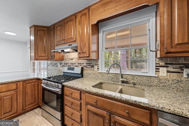 kitchen featuring a sink, under cabinet range hood, light stone countertops, backsplash, and stainless steel appliances