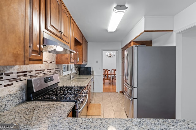 kitchen with under cabinet range hood, light stone countertops, brown cabinets, stainless steel appliances, and a sink