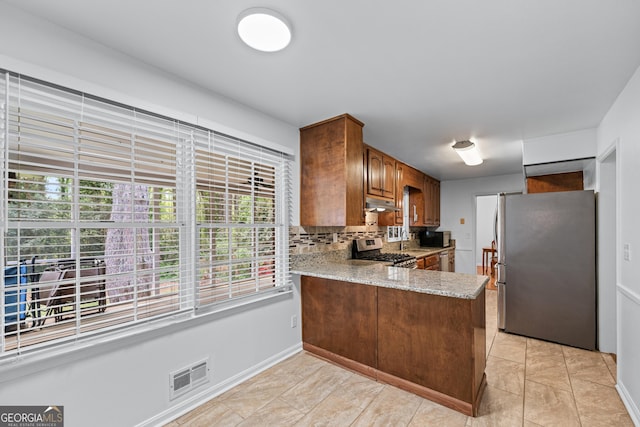 kitchen featuring a peninsula, light stone countertops, visible vents, decorative backsplash, and appliances with stainless steel finishes