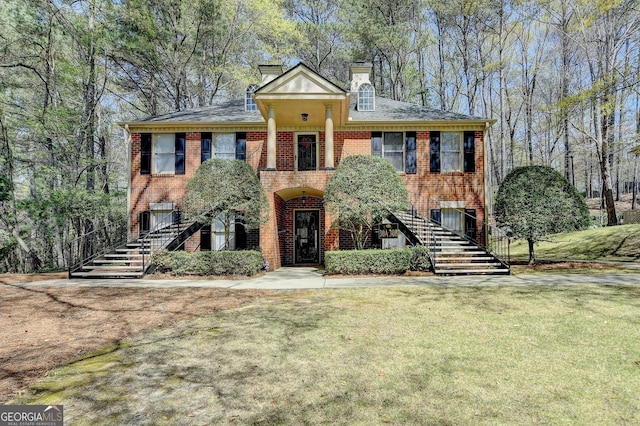 view of front of property featuring a front lawn, stairs, a chimney, and brick siding
