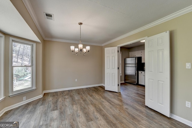 unfurnished dining area featuring visible vents, a chandelier, crown molding, and wood finished floors