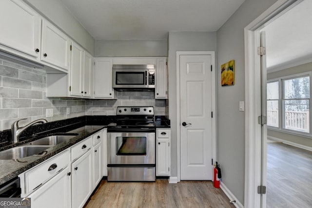kitchen with decorative backsplash, white cabinets, light wood finished floors, appliances with stainless steel finishes, and a sink