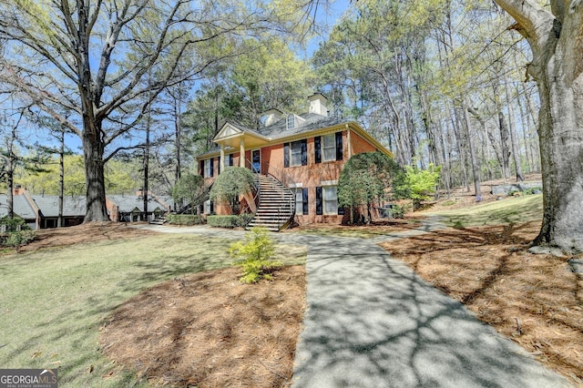 view of front of home featuring brick siding, a chimney, stairs, and a front yard