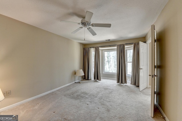 unfurnished room with a textured ceiling, baseboards, light colored carpet, and ceiling fan