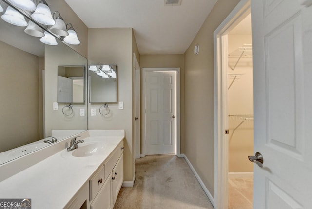 bathroom featuring baseboards, visible vents, a walk in closet, and vanity