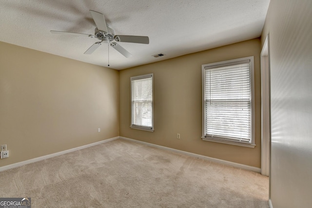 empty room with a textured ceiling, visible vents, a ceiling fan, and light carpet