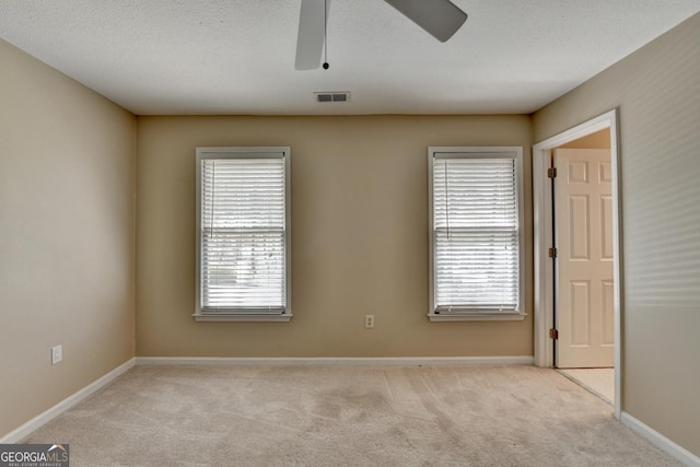 carpeted spare room with a wealth of natural light, visible vents, ceiling fan, and baseboards