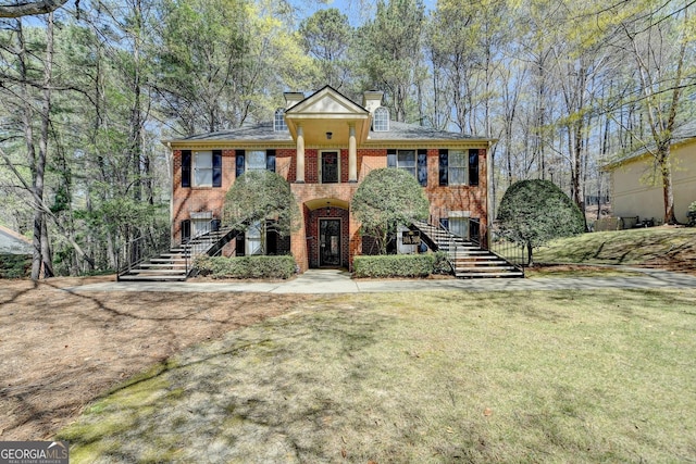 greek revival house with stairs, a chimney, brick siding, and a front yard