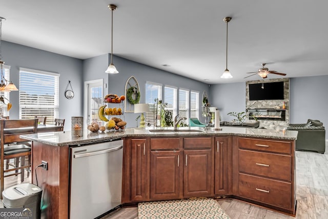 kitchen featuring a sink, ceiling fan, light wood-style flooring, stainless steel dishwasher, and stone countertops