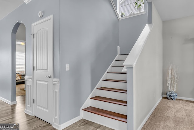 stairway with a towering ceiling, wood finished floors, baseboards, and arched walkways