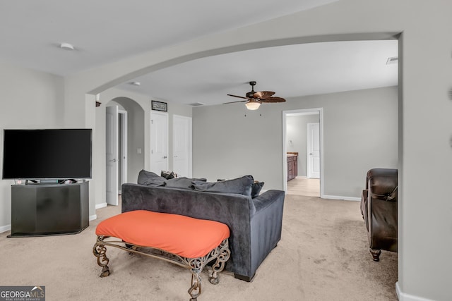 living room with baseboards, arched walkways, ceiling fan, and light carpet
