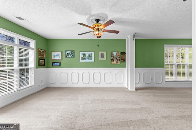 carpeted spare room with visible vents, a textured ceiling, ceiling fan, and a healthy amount of sunlight