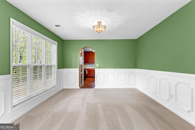 spare room with visible vents, wainscoting, light colored carpet, a textured ceiling, and arched walkways