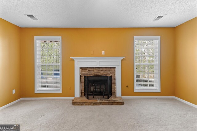 unfurnished living room featuring a stone fireplace, carpet flooring, a textured ceiling, and visible vents