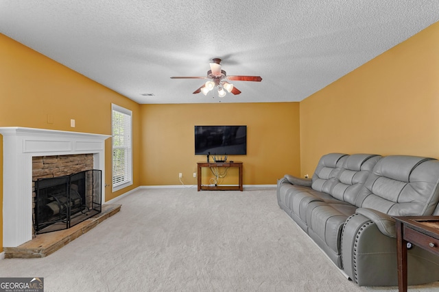 living room featuring baseboards, ceiling fan, a fireplace with raised hearth, a textured ceiling, and carpet flooring