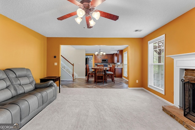 living area with a fireplace with raised hearth, a textured ceiling, stairway, and ceiling fan with notable chandelier