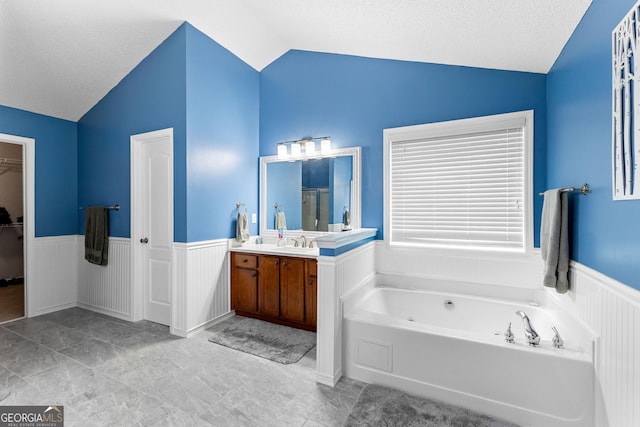 full bath featuring a garden tub, vanity, wainscoting, a textured ceiling, and vaulted ceiling
