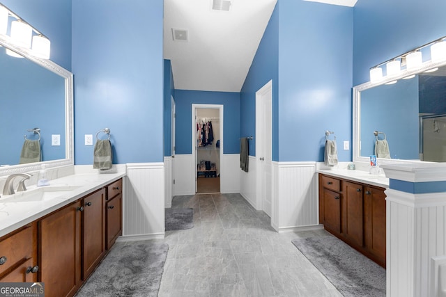 full bath featuring a sink, wainscoting, a walk in closet, and two vanities