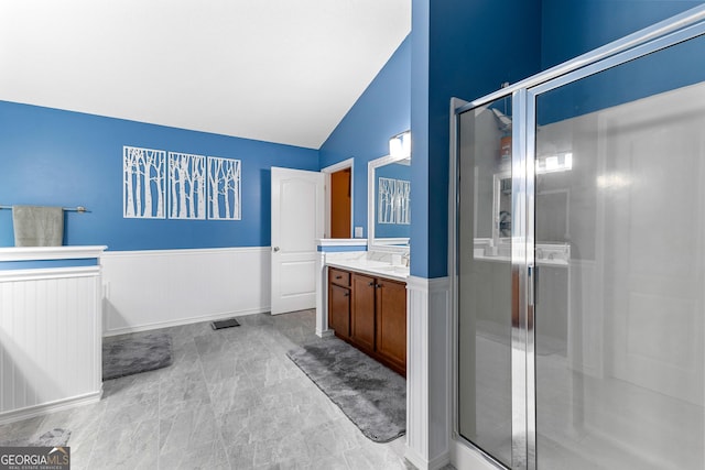 full bathroom with vanity, wainscoting, vaulted ceiling, and a shower stall