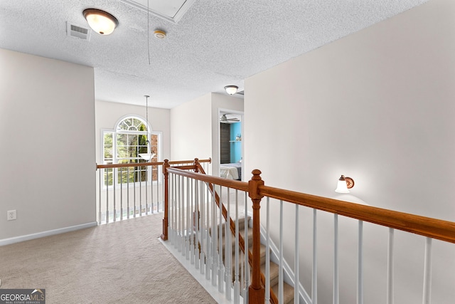 hall with carpet floors, a textured ceiling, attic access, baseboards, and visible vents