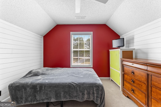bedroom featuring wooden walls, light carpet, a textured ceiling, and lofted ceiling