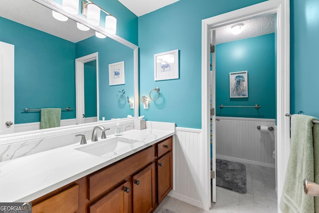 bathroom featuring wainscoting, vanity, toilet, a textured ceiling, and marble finish floor