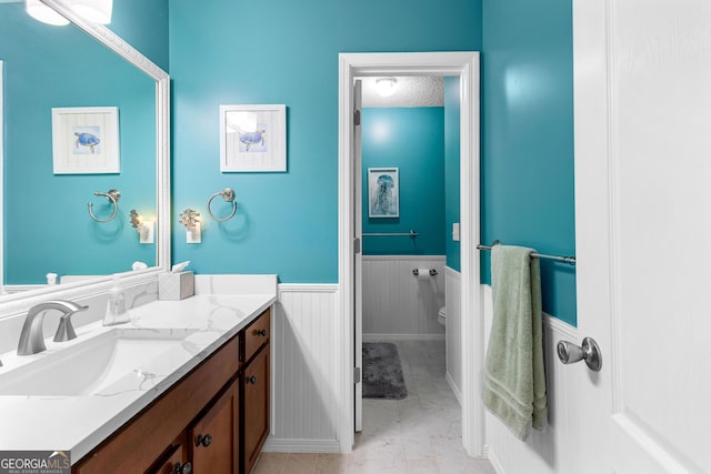 bathroom featuring vanity, marble finish floor, toilet, baseboards, and a wainscoted wall