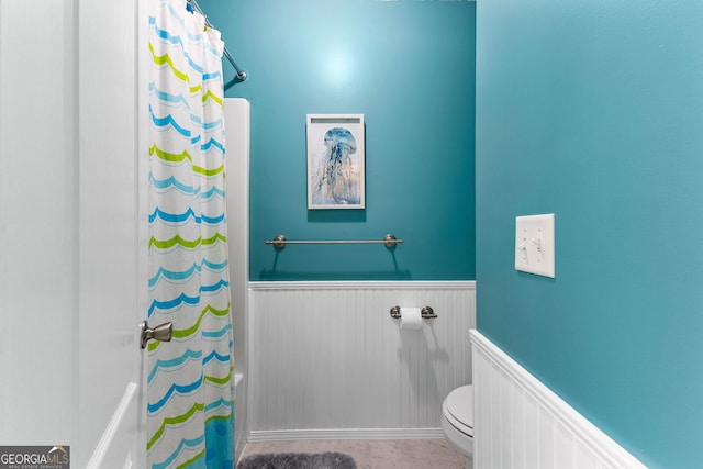 bathroom featuring a shower with shower curtain, a wainscoted wall, and toilet