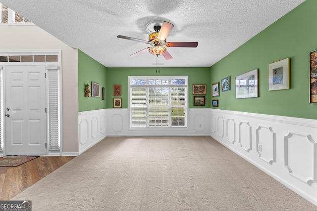 empty room with wainscoting, a textured ceiling, carpet, a ceiling fan, and wood finished floors