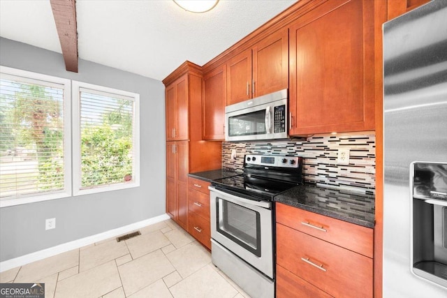 kitchen with decorative backsplash, baseboards, stainless steel appliances, dark stone countertops, and brown cabinetry