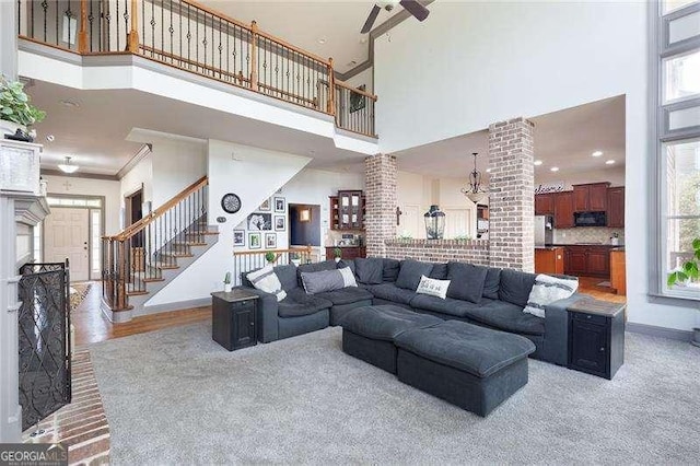 living room with crown molding, baseboards, stairs, a towering ceiling, and a ceiling fan