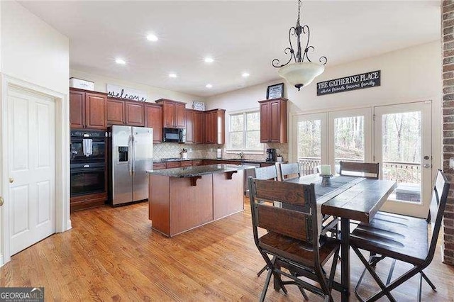 kitchen featuring backsplash, a kitchen island, light wood-style flooring, dark countertops, and black appliances