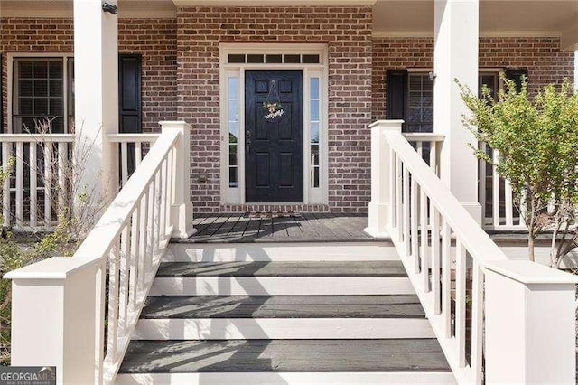 doorway to property featuring covered porch and brick siding
