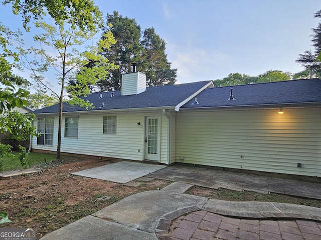 rear view of house with a chimney, a patio, and a shingled roof