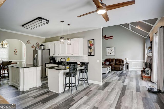 kitchen with a ceiling fan, a kitchen breakfast bar, dark countertops, arched walkways, and white cabinets
